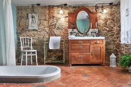 Grossräumiges Bad, in Terrakottaboden eingelassene Badewanne mit ländlichem Waschtischmöbel vor Natursteinwand
