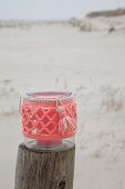 Candle lantern with coral-pink crocheted cover on wooden post on beach