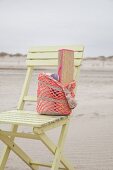 Gehäkelter Strandbeutel mit Bastmatte auf Holzstuhl am Strand