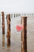 Candle lantern with coral-pink crocheted over hung from wooden post on beach