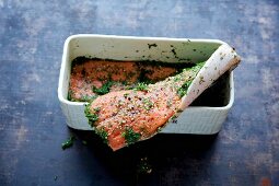 Graved lax being made: raw fillet of salmon being layered in a rectangular container with spices and dill