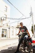 Man wearing jeans, T-shirt and sunglasses sitting on motorbike