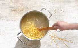 Spaghetti being cooked in a pot with a wooden spoon