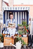 Woman sitting and reading in beach chair decorated with plants on balcony