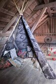 Floor cushions in teepee in rustic attic room with exposed wooden roof structure