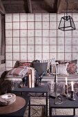 Candles and books on metal side table; cushions on comfortable bench against wall covered with vintage-style wallpaper