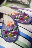 Slippers in Violett, bestickt mit Pailletten in Blumenform, im indischen Stil, auf gestreiftem Kissen