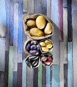 Various types of potatoes in sacks on a colourful wooden surface (seen from above)