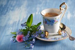 A coffee cup and a small bouquet of forget-me-not and daisies