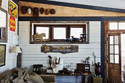 White wood-clad wall, vintage advertising panels and collectors' items on table in vintage-style interior