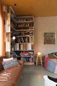 Leather couch in front of L-shaped bookcase made from reclaimed boards in corner of room with patchwork beanbag