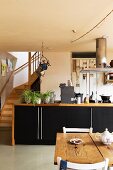 Dining area in front of kitchen counter with wooden frames and black doors; foot of staircase to one side