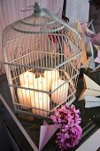 Lit pillar candles in disused birdcage next to pink hydrangea flowers