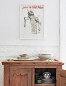 Crockery in antique half-height cabinet below modern printed poster