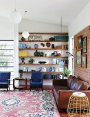 Brown leather couch and two blue armchairs in front of floating shelves in niche in corner of living room