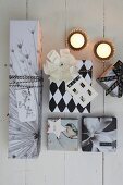 Gifts wrapped in black and white paper and lit tealights on white wooden floor
