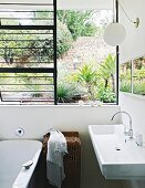 Modernes Waschbecken neben offenem Fenster mit Gartenblick
