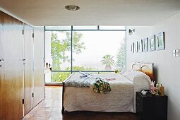 Box-spring bed and wooden fitted wardrobes in bedroom with view of garden through glass wall