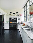 Black and white kitchen with long counter below bank of windows and black vinyl floor