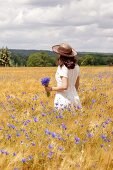 A woman in a corn field with a bunch of cornflowers