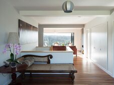 Antique chaise longue in foyer against masonry stair balustrade with view of lounge area and woodland landscape