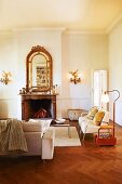 Traditional room with old fireplace, retro standard lamp, pale armchairs on herringbone parquet floor an antique framed mirror