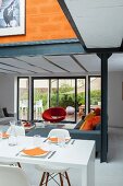 Open-plan living area with white dining table, corner sofa and designer armchair in front of sliding terrace doors