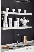 Detail of kitchen counter; white worksurface with integrated sinks below white floating shelves on black-painted wall