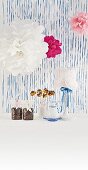 Decorated afternoon coffee table - paper pompoms, table lamp with doily lampshade, cake pops and packaged coffee beans against blue stripes back wall