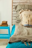 Selbstgebautes Bett mit rustikalem Kopfende aus Holz und rustikaler Leinenbettwäsche