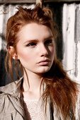 A young woman wearing a lace blouse and a leather gillet standing against a corrugated iron wall