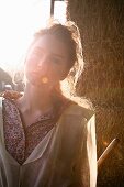 A young woman standing by hay bales (photo taken against the light)