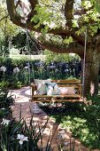 DIY wooden swing bench hung from tree in summer garden