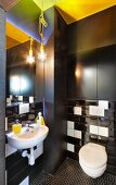 Modern toilet with black installations, black and white glossy wall tiles and yellow accents