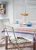 Teapot and mugs on table with striped tablecloth and pale green folding chairs