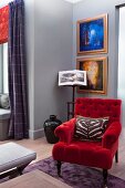 Armchair with red velvet cover in front of gilt-framed artworks on grey-painted wall