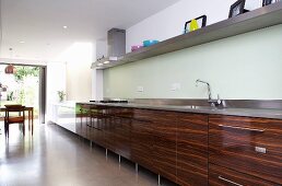 Long, wood-effect kitchen counter below shelf in kitchen with dining area in background in front of terrace doors