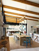 Long wooden dining table and chairs on sisal rug under wood-beamed ceiling