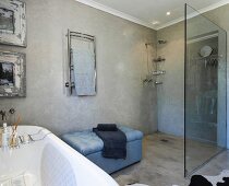 Pale blue upholstered bench between walk-in shower with glass screen and bathtub with bath caddy