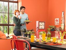Junges Paar vor gedecktem Tisch mit Drinks und Vorspeisen in orangefarbenem Essraum