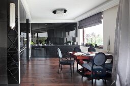 Dining area with antique chairs in elegant living room with black, fitted cupboards, dark wooden floor and white stucco frieze