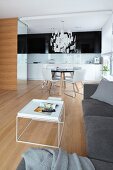 Nest of white coffee tables, grey sofa combination and dining area in background in open-plan kitchen