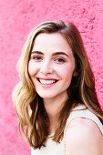 A portrait of a dark blonde woman in front of a pink wall