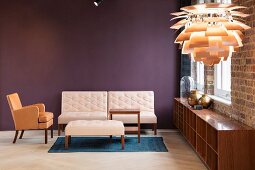 Sessel mit hellbraunem Bezug und Sofa mit Polstertisch hellbezogen vor violett getönter Wand, im Vordergrund Artischokke Pendelleuchte