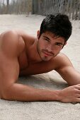 A young, topless man lying in the sand