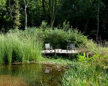 Idyllischer Gartenplatz auf sonnenbeschienenem Holzdeck am Teichrand