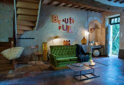 Vintage sofa with green velvet cover next to foot of winding staircase in open-plan interior of rustic country house