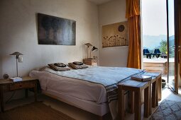 Ethnic-style bedroom with three wooden stools at foot of bed and view through open French windows