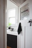 View of tiled washstand with black base unit seen through open bathroom door in period apartment