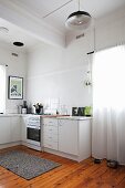 Simple, white base units, retro lamp and old wooden floor in kitchen